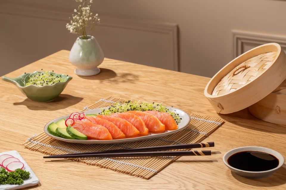 Sashimi de salmón con palillos y cesta de vapor sobre una mesa clara.