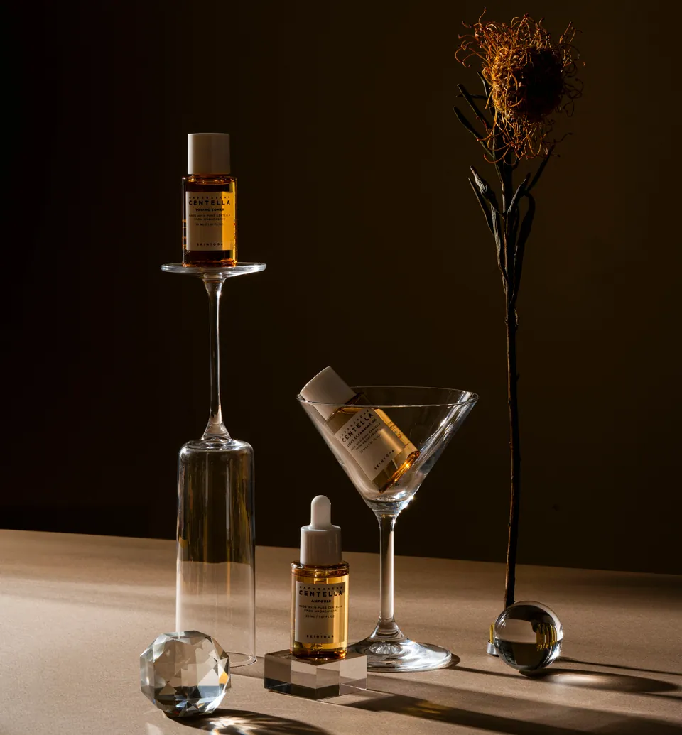 Frascos de sérum sobre copas de cristal y una flor seca, fondo marrón.