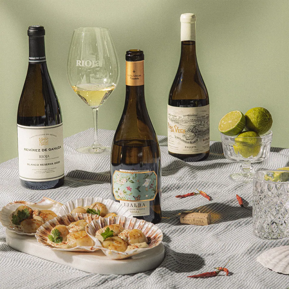 Vinos blancos con ostras sobre mantel blanco, fondo verde salvia.