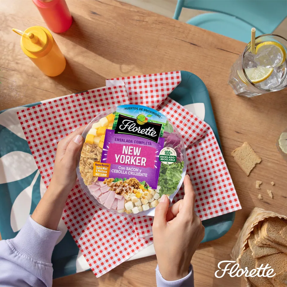 Manos que sostienen una ensalada Florette sobre mantel de cuadros rojos.